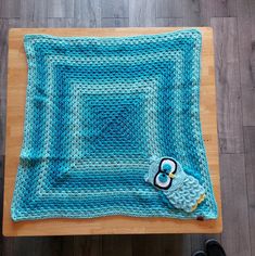 a blue crocheted blanket sitting on top of a wooden table next to a pair of black shoes