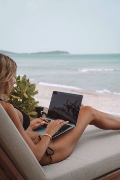 a woman sitting in a chair on top of a laptop computer next to the ocean