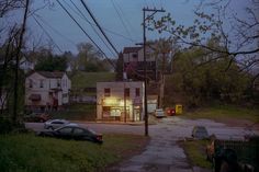 an empty street at night with cars parked on the side and buildings in the background