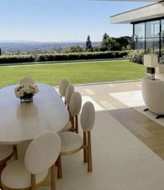 a dining room table with white chairs in front of a large window overlooking a field