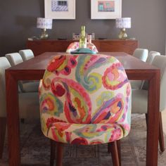 a dining room table with colorful chairs and pictures on the wall