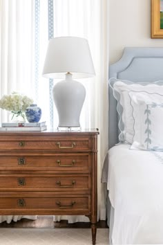 a white lamp sitting on top of a wooden dresser next to a blue and white bed