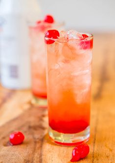 two glasses filled with ice and cherries on top of a wooden table