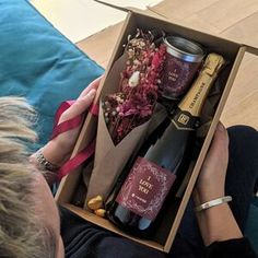 a woman is holding an open box with some wine and other items in it while sitting on a couch