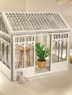 a doll house with a white roof and some plants in the window sill next to a potted plant