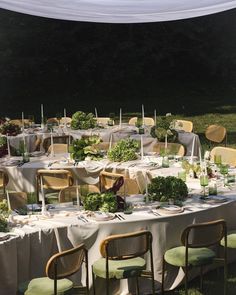 an outdoor table set up with chairs and tables covered in cloths, surrounded by greenery