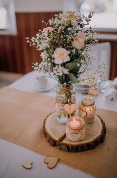 mason jars filled with flowers and candles on a wooden slice at a wedding reception table