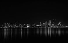 black and white photograph of the city skyline at night from across the water with reflections in the water