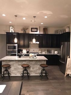 a kitchen with black cabinets and stools in front of an island counter top that has three bar stools on it