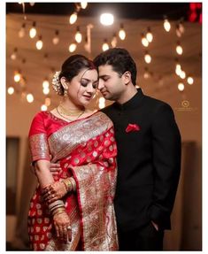 a man and woman standing next to each other wearing red and gold sarees