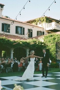 a bride and groom dancing on a checkered floor in front of an outdoor venue