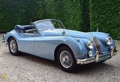 an old blue sports car parked in front of a hedge