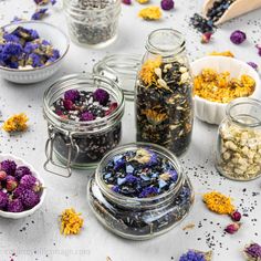 several jars filled with different types of flowers and herbs next to spoons on a table