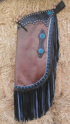 a cowgirl's purse with fringes and blue beads on it sitting in hay