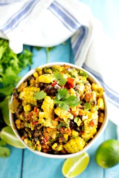 a white bowl filled with corn and black beans next to cilantro, lime wedges