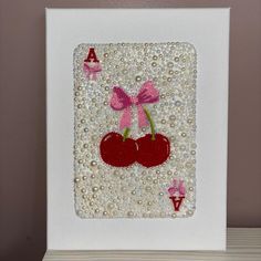 a white frame with a pink bow and two cherries on it, sitting on a shelf