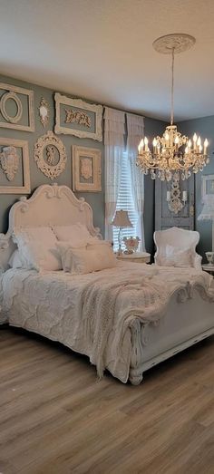 a white bed sitting in a bedroom next to a chandelier on a wooden floor