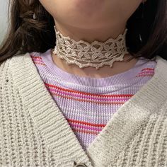 a close up of a woman wearing a white sweater and pink striped shirt with a lace choker on her neck