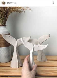 a person is holding their hand out to some sculptures on a wooden table next to a vase with dry grass in it