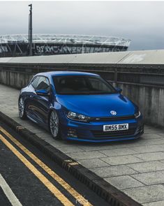 a blue car parked on the side of a road next to a bridge and building