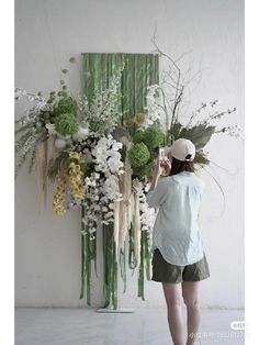 a woman standing in front of a wall with lots of flowers and plants on it