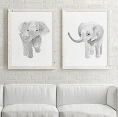 three paintings of elephants hang on the wall above a white couch in front of a brick wall