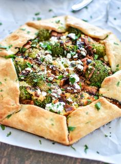 a pizza with broccoli, cheese and other toppings is on a piece of parchment paper