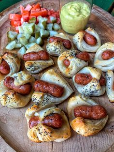 some hot dogs and vegetables on a wooden platter with dipping sauce in the background