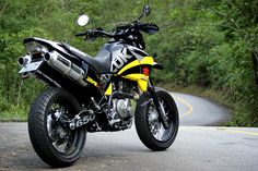 a yellow and black motorcycle is parked on the side of the road in front of some trees