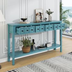 a blue console table with three drawers and two plants on top, against a white wall