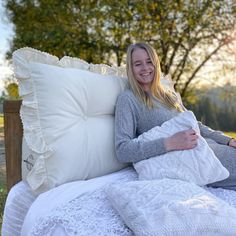 a woman is sitting on a bed with pillows and blankets around her, smiling at the camera