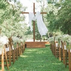 an outdoor ceremony setup with white flowers and greenery on the grass, in front of a wooden cross