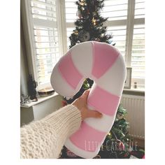 a person holding up a candy cane pillow in front of a christmas tree and window