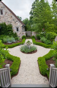 an outdoor garden with stone walls and gravel path leading to the front door, surrounded by greenery