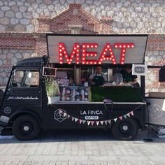 a food truck parked in front of a building with a neon sign on it's side