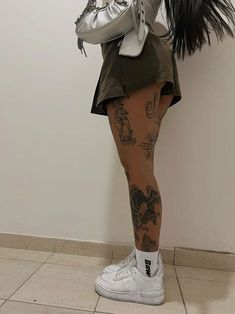 a woman with tattoos is standing in front of a wall and holding a handbag