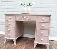 a pink desk with two white vases on top of it and a wooden floor