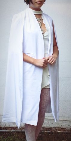 a woman in tights and a white cape is standing on the grass with her hands behind her back