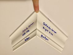 a hand is pointing at three white folded paper pieces with writing on them that read outside corner, right in the center and bottom