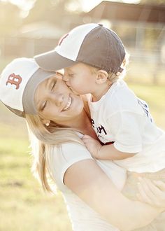 a woman is holding a small boy in her arms and he is wearing a baseball cap