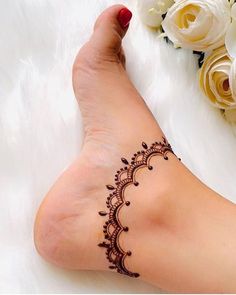 a woman's foot with a henna tattoo on it and flowers in the background