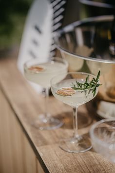 two martini glasses with rosemary garnish sit on a wooden table