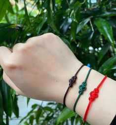 a woman's arm with three bracelets on top of it and green leaves in the background