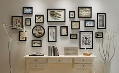 a white desk topped with lots of pictures and framed art on the wall next to a lamp