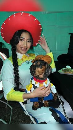 a woman is holding a small dog in her lap while wearing a costume and hat