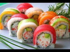 several sushi rolls are arranged on a white plate with green and orange garnishes