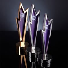 three trophies sitting next to each other on top of a black table with silver and gold trim