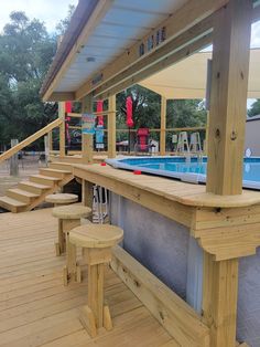 a wooden deck next to a swimming pool with benches and stools on the side