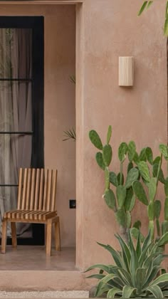 a wooden chair sitting in front of a window next to a green plant and potted cactus