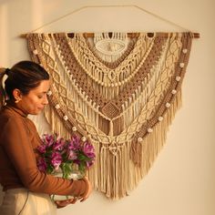 a woman holding a bouquet of flowers in front of a macrame wall hanging